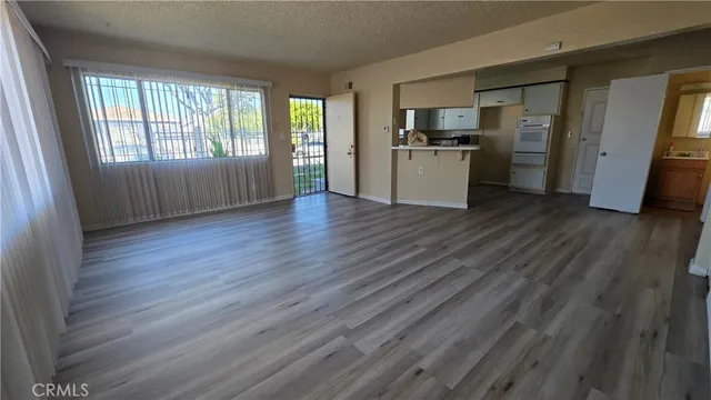 an empty room with wooden floor and a kitchen