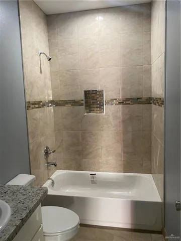a bathroom with a granite countertop bathtub shower sink vanity and toilet