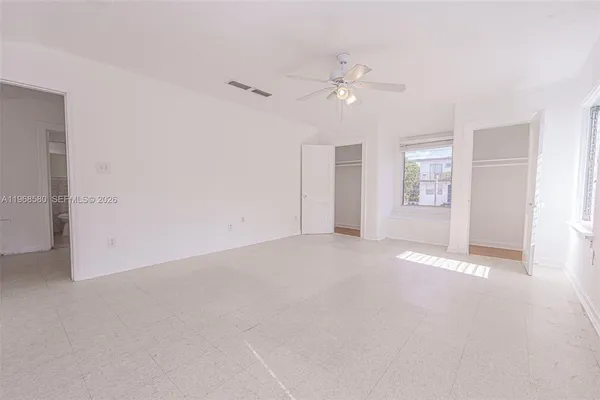 an empty room with chandelier fan and windows