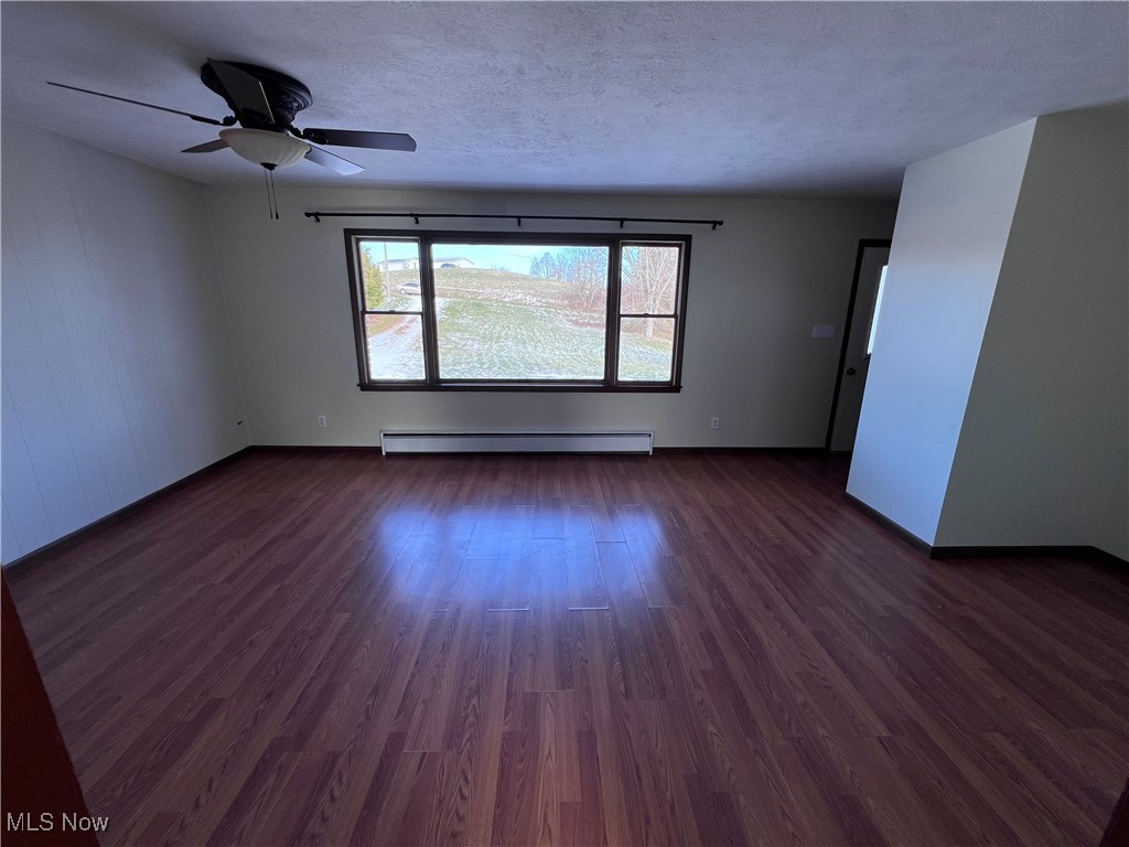 56376 Jordan Run Road Bellaire, OH 43906 - Photo 13 of 45 Empty room with ceiling fan, dark hardwood / wood-style flooring, a textured ceiling, and a baseboard heating unit