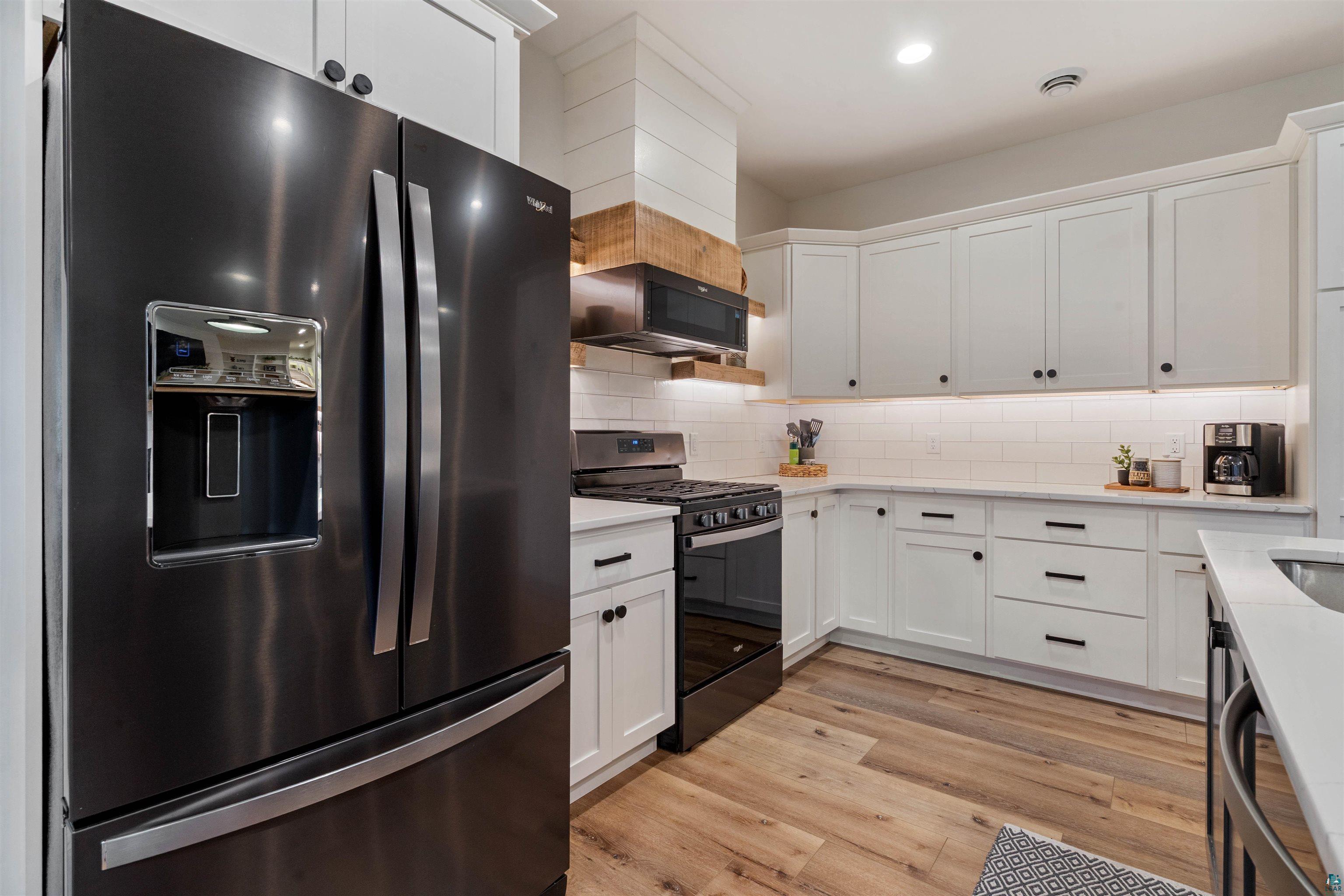 59 East Riverside Road Esko, MN 55733 - Photo 13 of 48 Kitchen with black appliances, white cabinetry, light wood-style flooring, backsplash, and light stone counters
