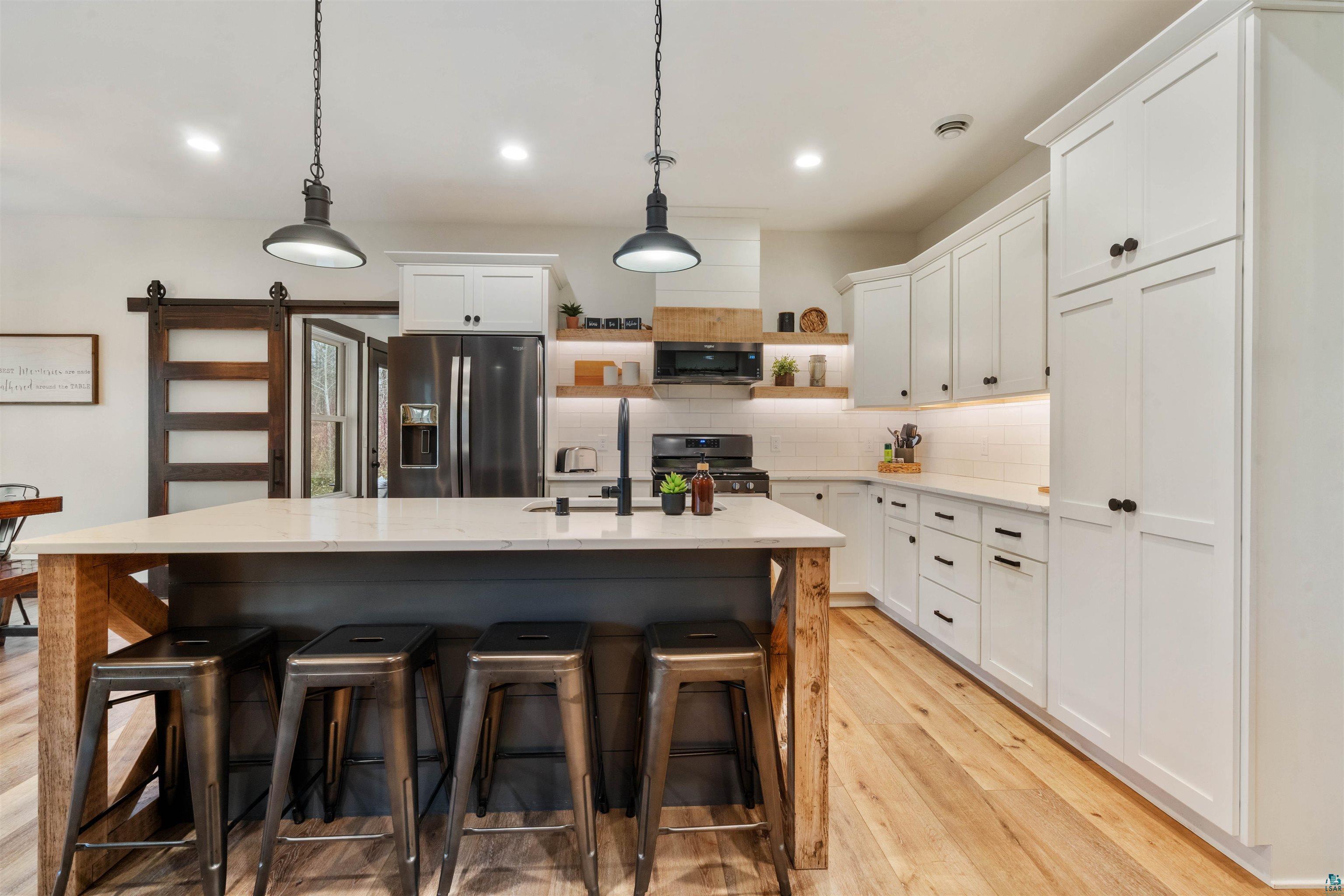 59 East Riverside Road Esko, MN 55733 - Photo 5 of 48 Dual tone kitchen featuring open shelves, stainless steel appliances, an island with sink, pendant lighting, and light wood finished floors