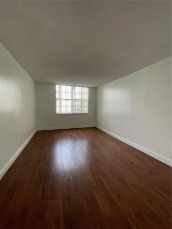 a view of an empty room with wooden floor and window