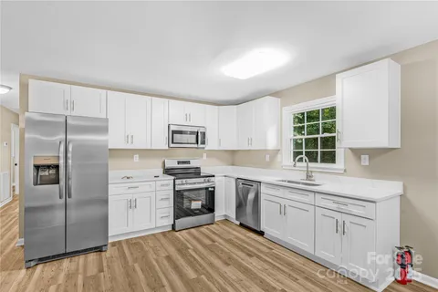 a kitchen with stainless steel appliances granite countertop a stove a sink dishwasher a refrigerator and white cabinets with wooden floor
