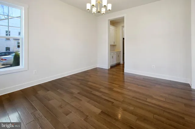 an empty room with wooden floor chandelier and windows