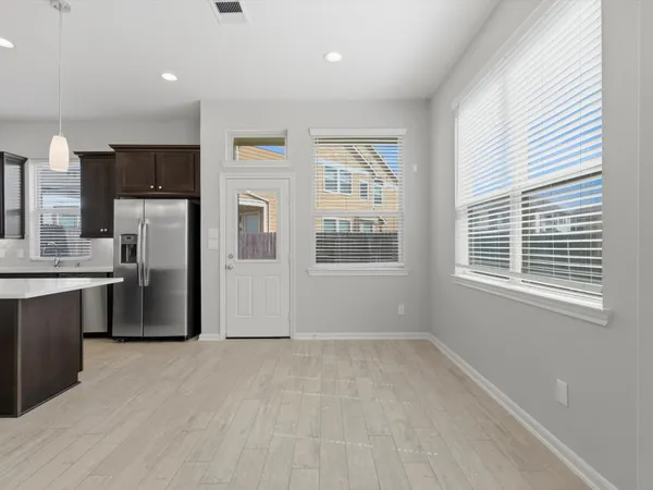 an empty room with chandelier fan and kitchen view