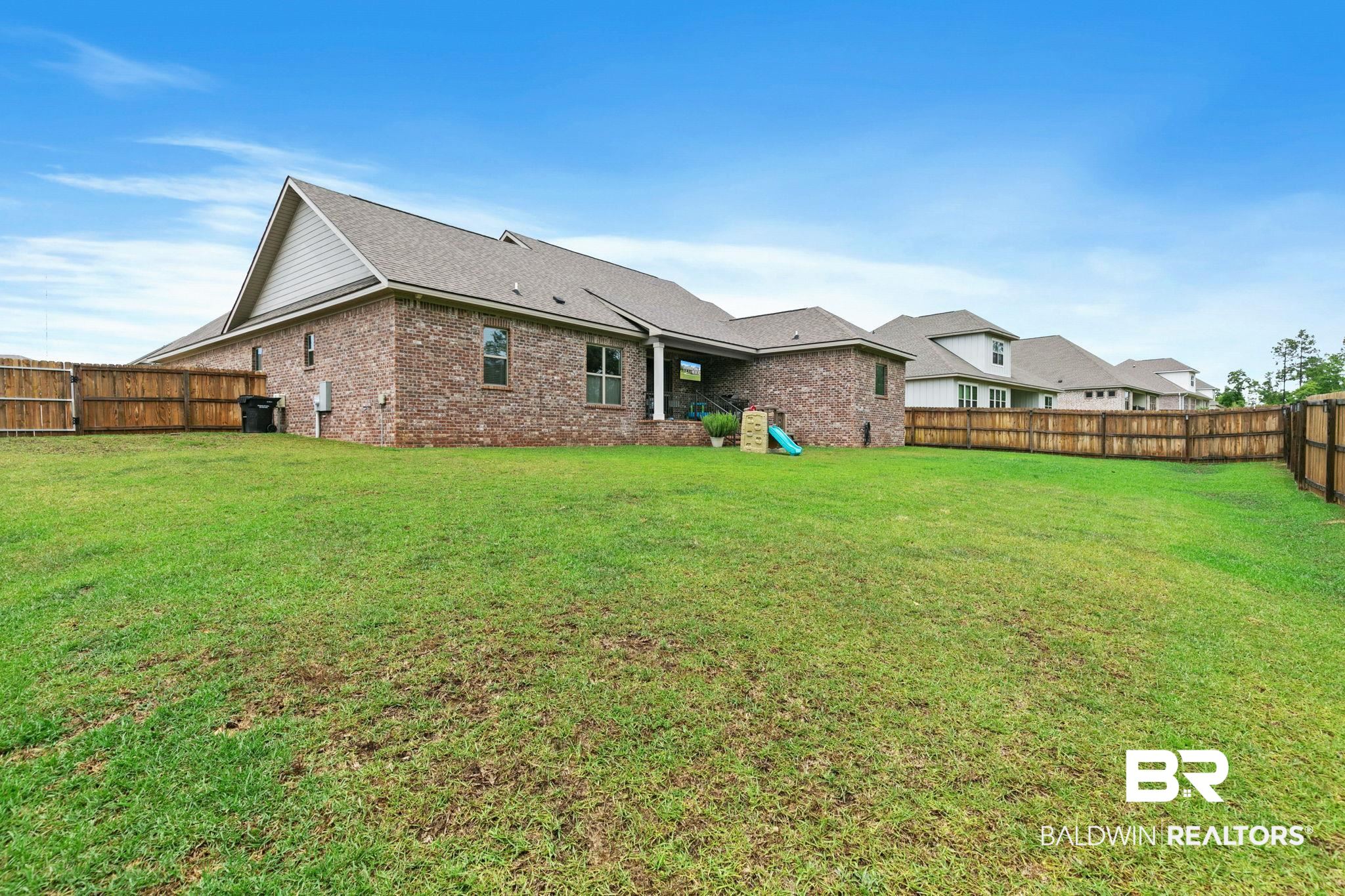 13233 Ibis Boulevard Daphne, AL 36527 - Photo 62 of 100 Expansive backyard featuring a manicured lawn, full privacy fencing, brick exterior, covered patio, and multi-pane windows