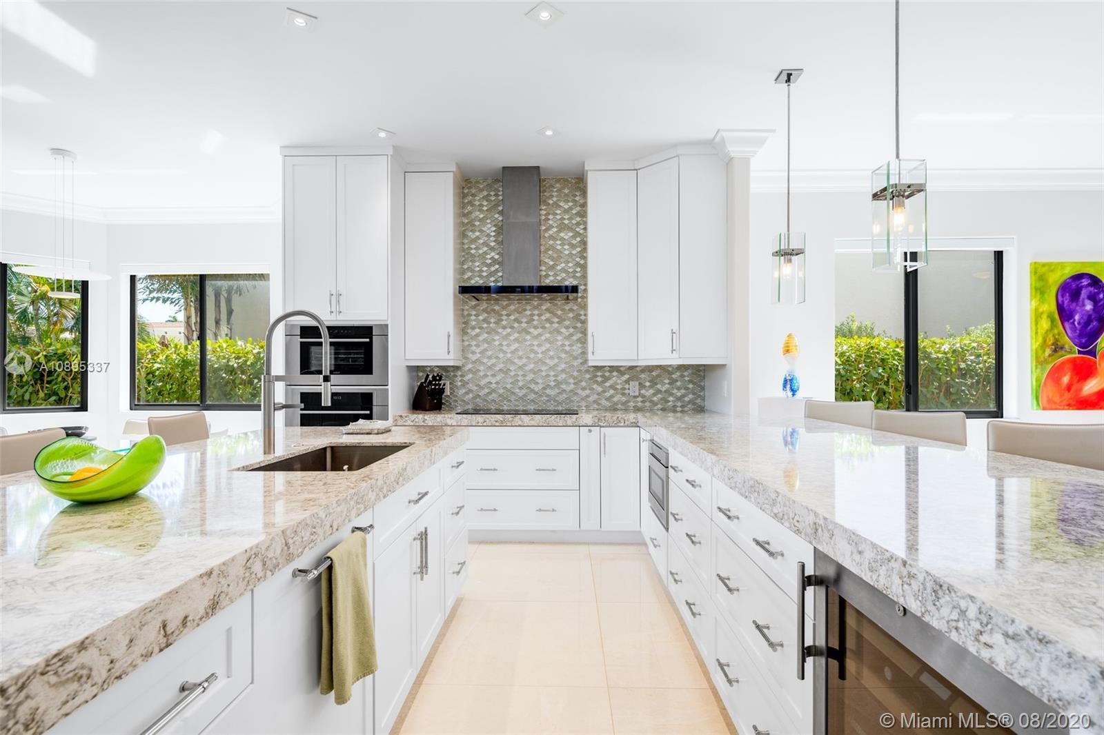 a large white kitchen with granite countertop a sink a counter top space and stainless steel appliances