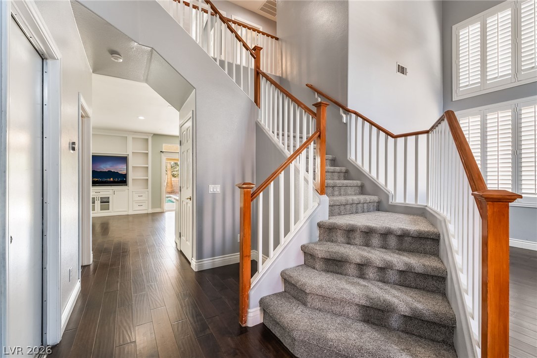 261 Timber Hollow Street Henderson, NV 89012 - Photo 9 of 51 A grand, carpeted staircase with wood railings creates a welcoming entry, complemented by dark wood flooring.