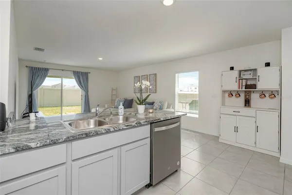 a large white kitchen with granite countertop a sink white cabinets and a dishwasher next to a window