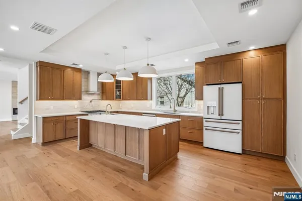 a kitchen with stainless steel appliances granite countertop a refrigerator a stove a sink and white cabinets with wooden floor