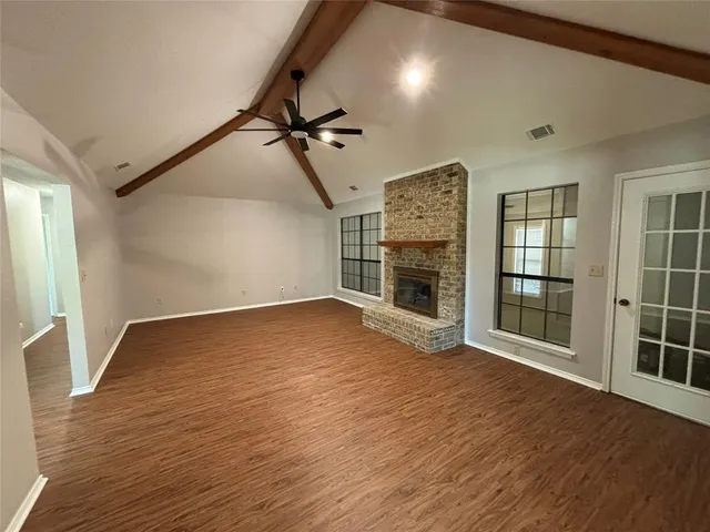 a view of an empty room with wooden floor fireplace and a window
