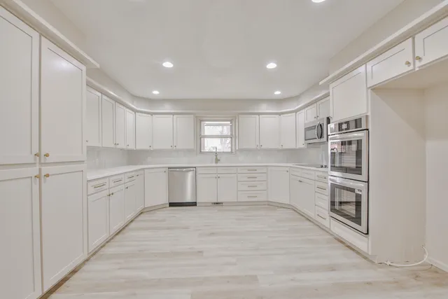 a large white kitchen with stainless steel appliances granite countertop a large counter top and a stove top oven