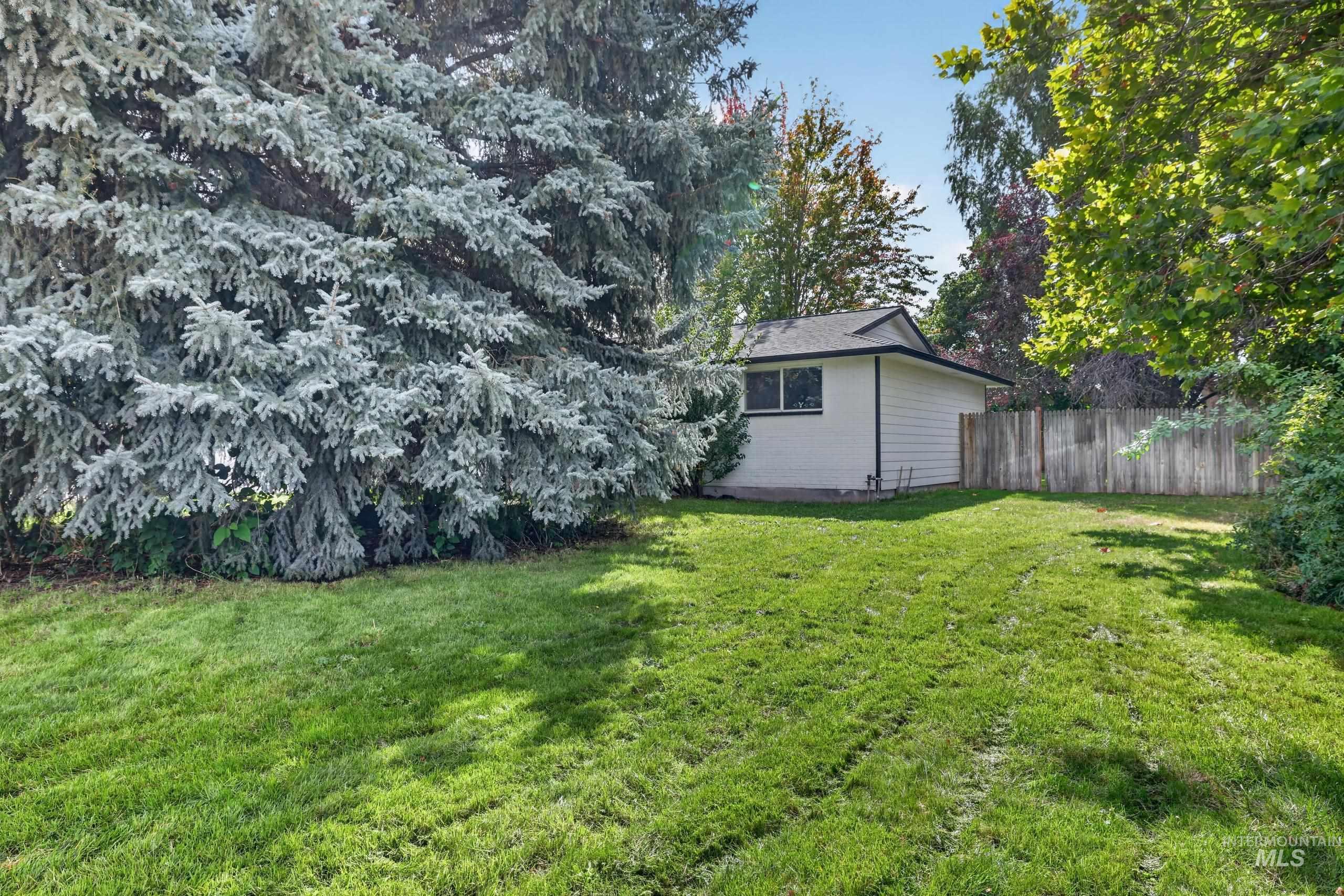 9055 West Highlander Road Boise, ID 83709 - Photo 31 of 39 Expansive grassy yard with mature trees, a detached structure featuring white siding, and a wood fence