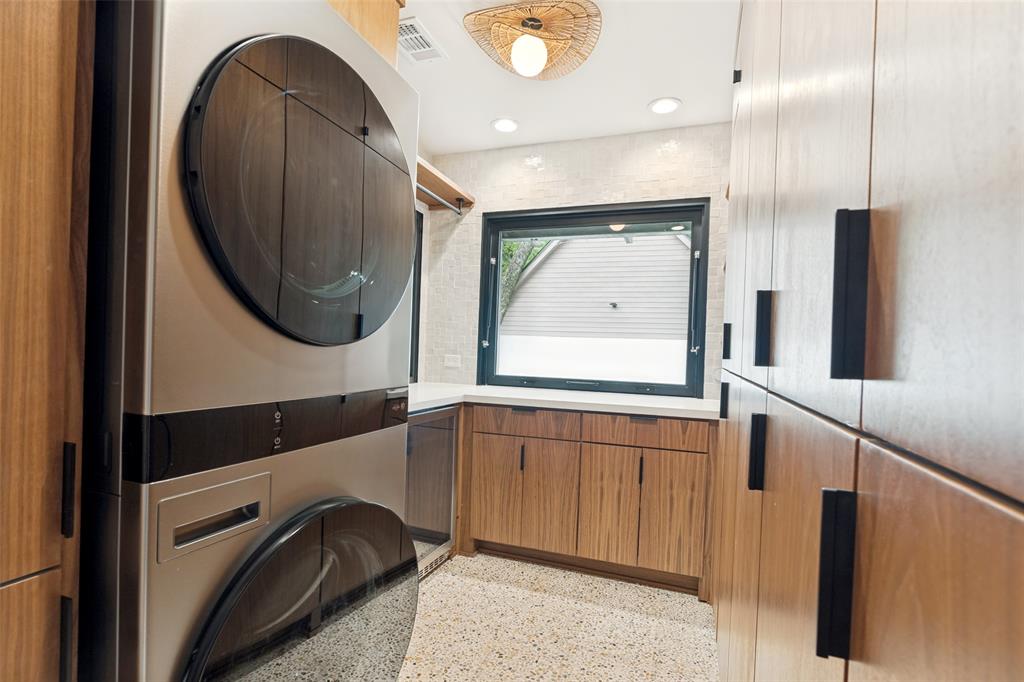 4325 Pomona Road Dallas, TX 75209 - Photo 11 of 23 Dedicated laundry area featuring stacked appliances, abundant wood-finish cabinetry with black hardware, a light-colored countertop, and a large horizontal window