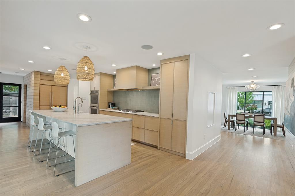 4325 Pomona Road Dallas, TX 75209 - Photo 8 of 23 Modern kitchen featuring a large waterfall island with integrated seating, light wood-finish cabinetry, a built-in range hood, a tiled backsplash, and recessed lighting