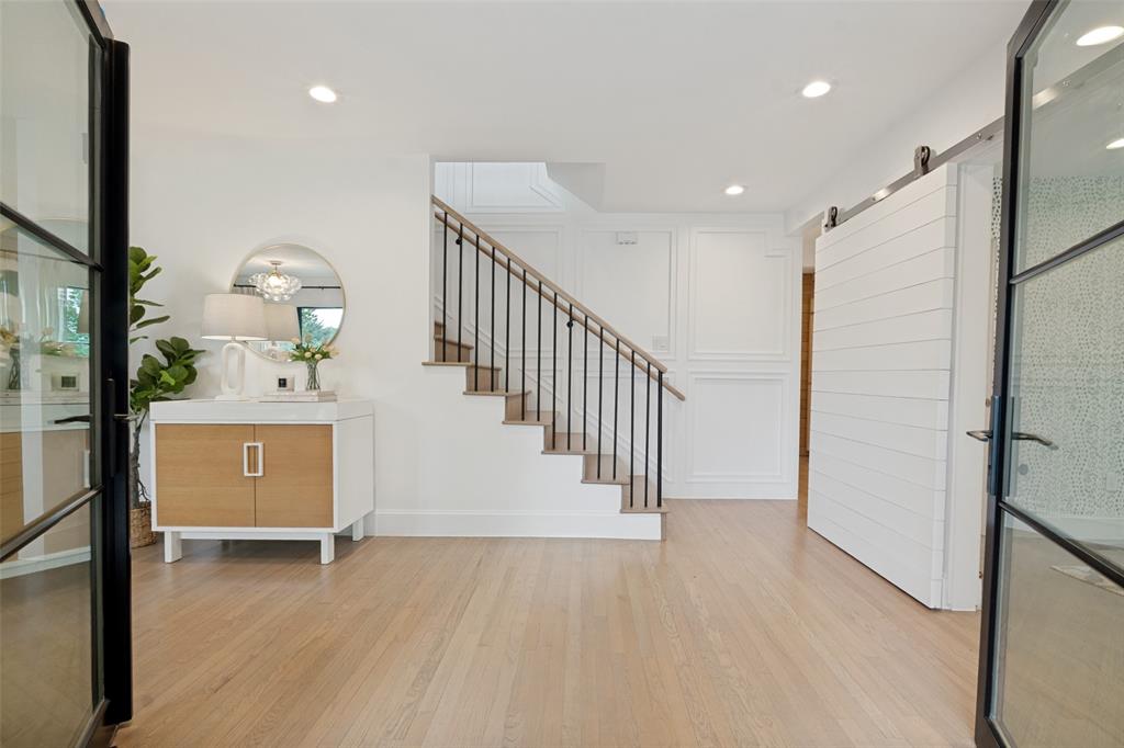 4325 Pomona Road Dallas, TX 75209 - Photo 9 of 23 Entryway featuring light wood-finish flooring, a staircase with black metal balusters and a light wood handrail, recessed lighting, and a white shiplap barn door