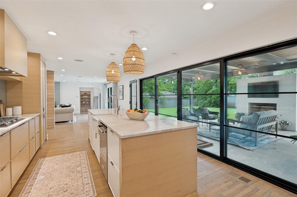 4325 Pomona Road Dallas, TX 75209 - Photo 10 of 23 Open-concept kitchen featuring light wood cabinetry, stone countertops, a large island with sink, stainless steel appliances, and wood-finish flooring
