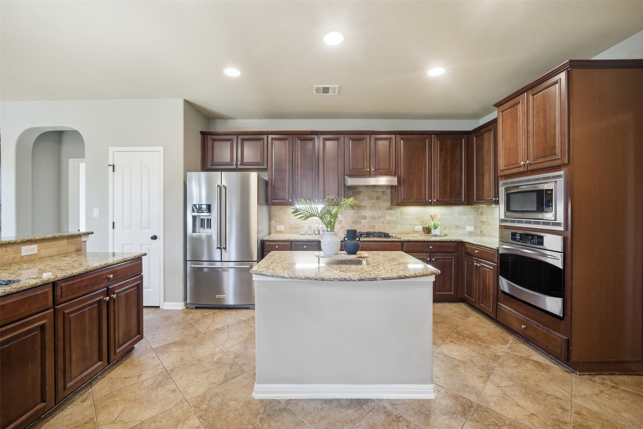 16100 Spillman Ranch Loop Austin, TX 78738 - Photo 19 of 39 Kitchen featuring stainless steel appliances, light stone counters, recessed lighting, arched walkways, and a kitchen island