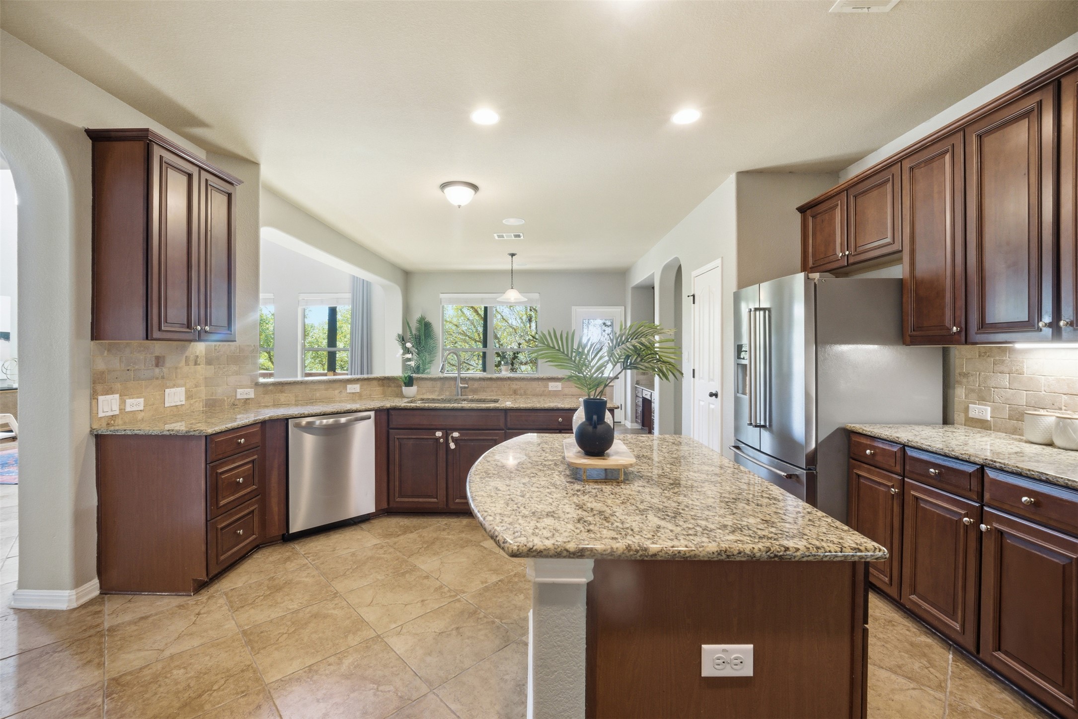 16100 Spillman Ranch Loop Austin, TX 78738 - Photo 20 of 39 Kitchen with backsplash, a kitchen island, arched walkways, light stone counters, and stainless steel appliances