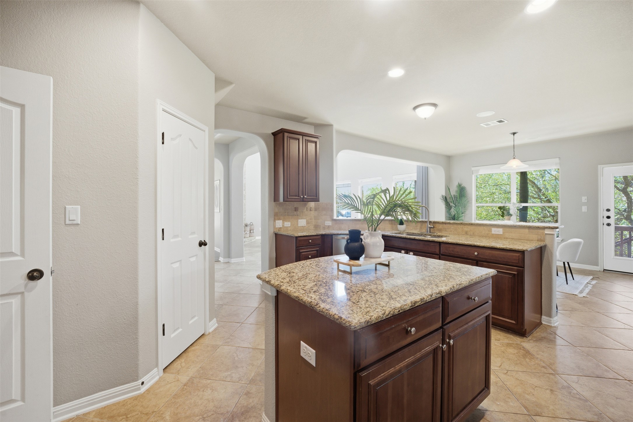 16100 Spillman Ranch Loop Austin, TX 78738 - Photo 21 of 39 Kitchen with a kitchen island, arched walkways, a peninsula, light stone countertops, and decorative light fixtures