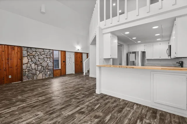 a view of an empty room with wooden floor and a kitchen