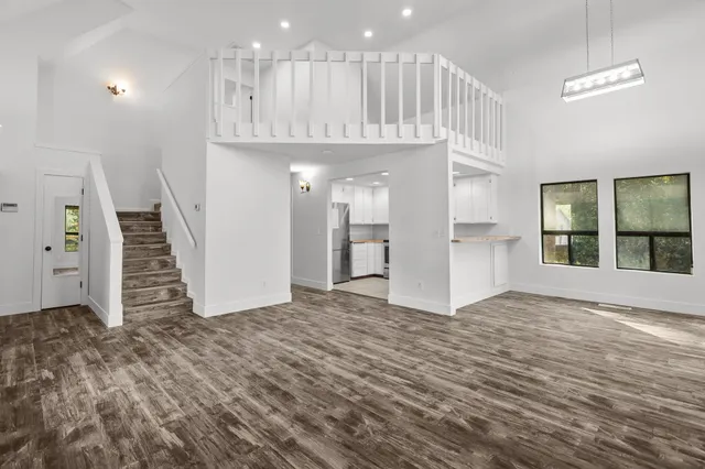 a view of an empty room with wooden floor and kitchen view