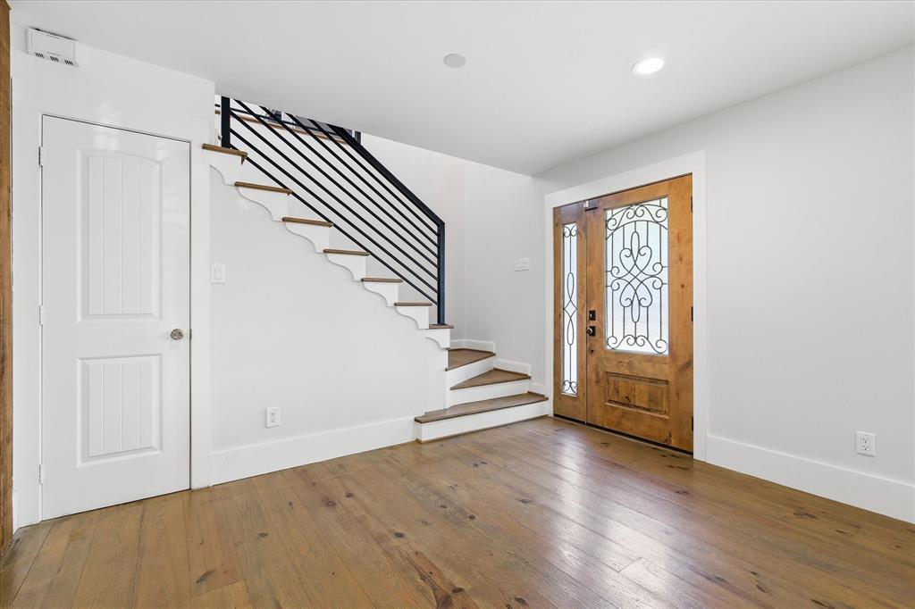 4310 Forest Bend Road Dallas, TX 75244 - Photo 6 of 40 Entryway featuring wood-finish flooring, a wood-panel front door with decorative ironwork and sidelights, a staircase with wood treads and a black metal railing, a white paneled door, and recessed lighting