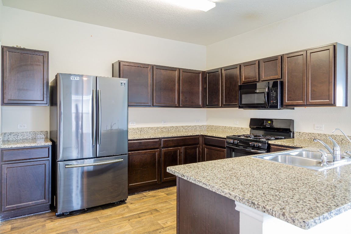 15225 Harkness Pass Austin, TX 78725 - Photo 7 of 23 a kitchen with kitchen island granite countertop stainless steel appliances and wooden cabinets