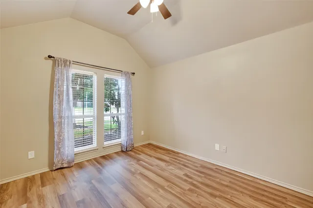 an empty room with wooden floor chandelier fan and windows