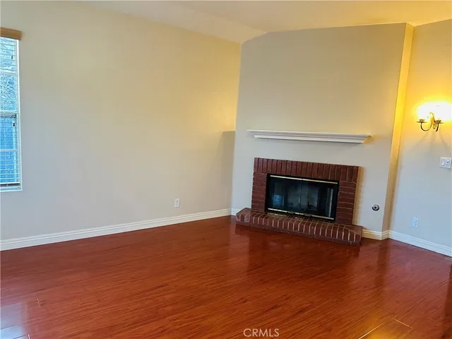 a view of an empty room with wooden floor a fireplace and a window