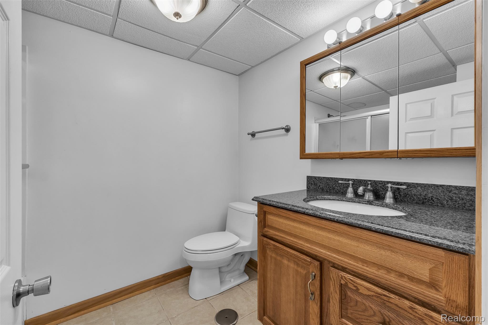 7000 Woonsocket Street Canton, MI 48187 - Photo 55 of 65 Bathroom featuring a wood-finish vanity with a built-in sink, dark stone-finish countertop, and a mirrored medicine cabinet