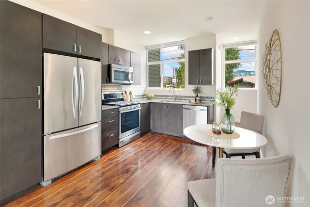 a kitchen with stainless steel appliances granite countertop a refrigerator a stove a sink a dining table and chairs with wooden floor