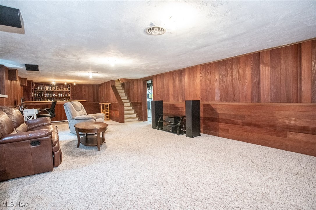 13740 Old Pleasant Valley Road Cleveland, OH 44130 - Photo 24 of 28 Carpeted living room featuring stairway, wood walls, a textured ceiling, visible vents, and a dry bar