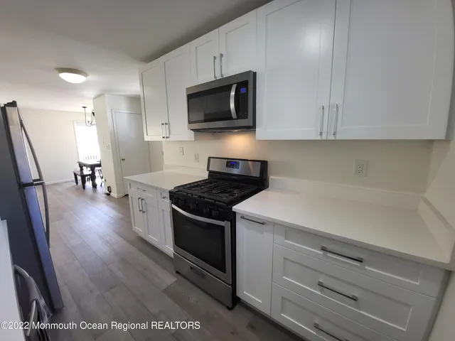 a kitchen with stainless steel appliances a stove a microwave a refrigerator a stove and white cabinets with wooden floor