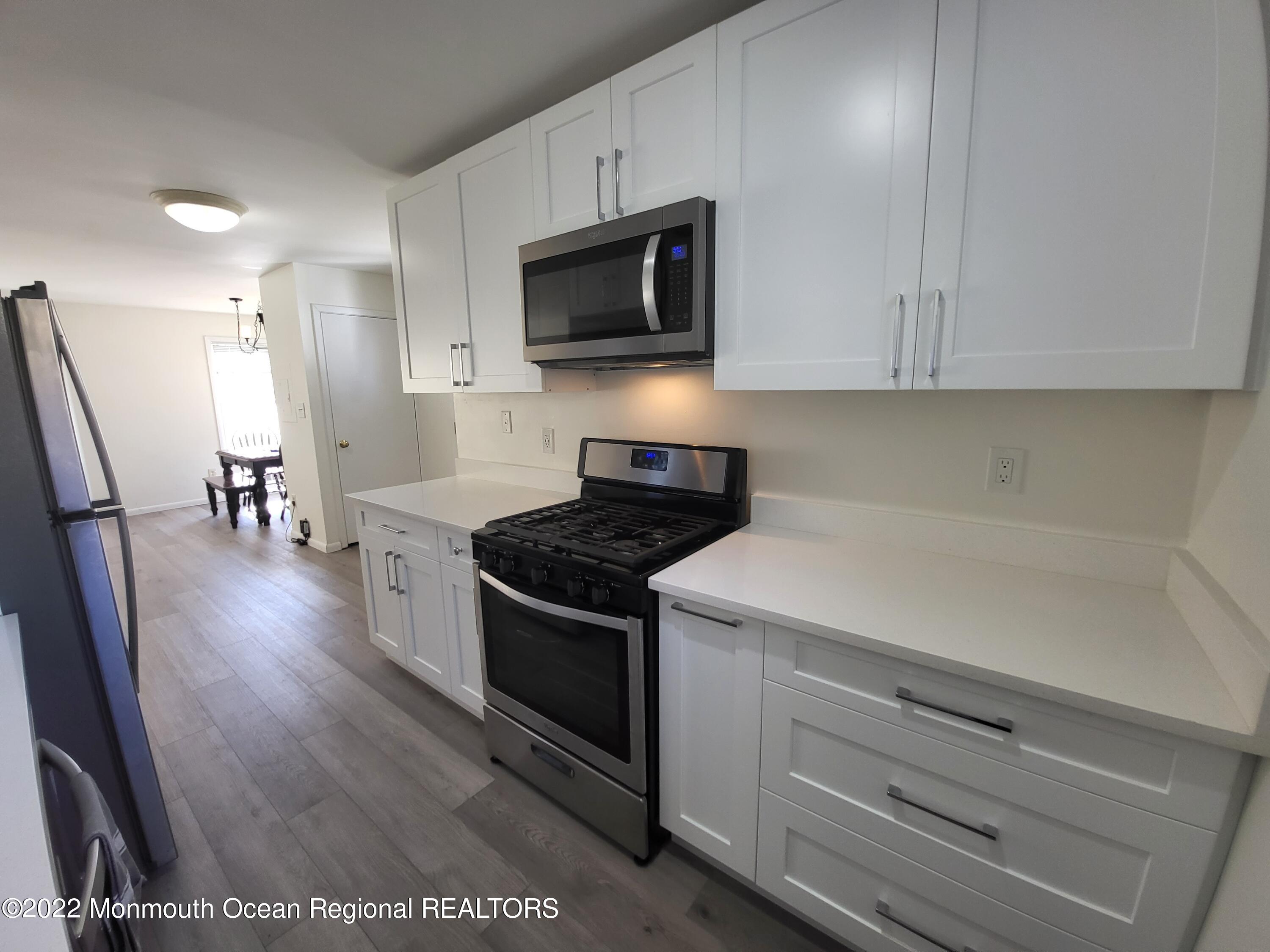 1703 A Street, Unit REAR Belmar, NJ 07719 - Photo 11 of 29 a kitchen with stainless steel appliances a stove a microwave a refrigerator a stove and white cabinets with wooden floor