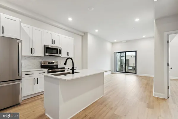 a kitchen with stainless steel appliances granite countertop a refrigerator a sink dishwasher a stove top oven a refrigerator and white cabinets with wooden floor