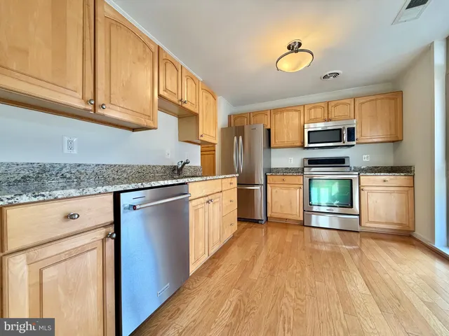 a kitchen with granite countertop a stove top oven a sink dishwasher and a refrigerator with wooden floor