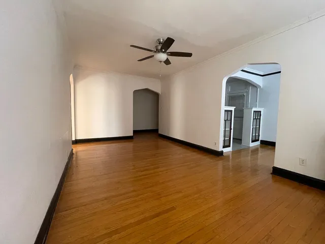 an empty room with wooden floor a ceiling fan and windows