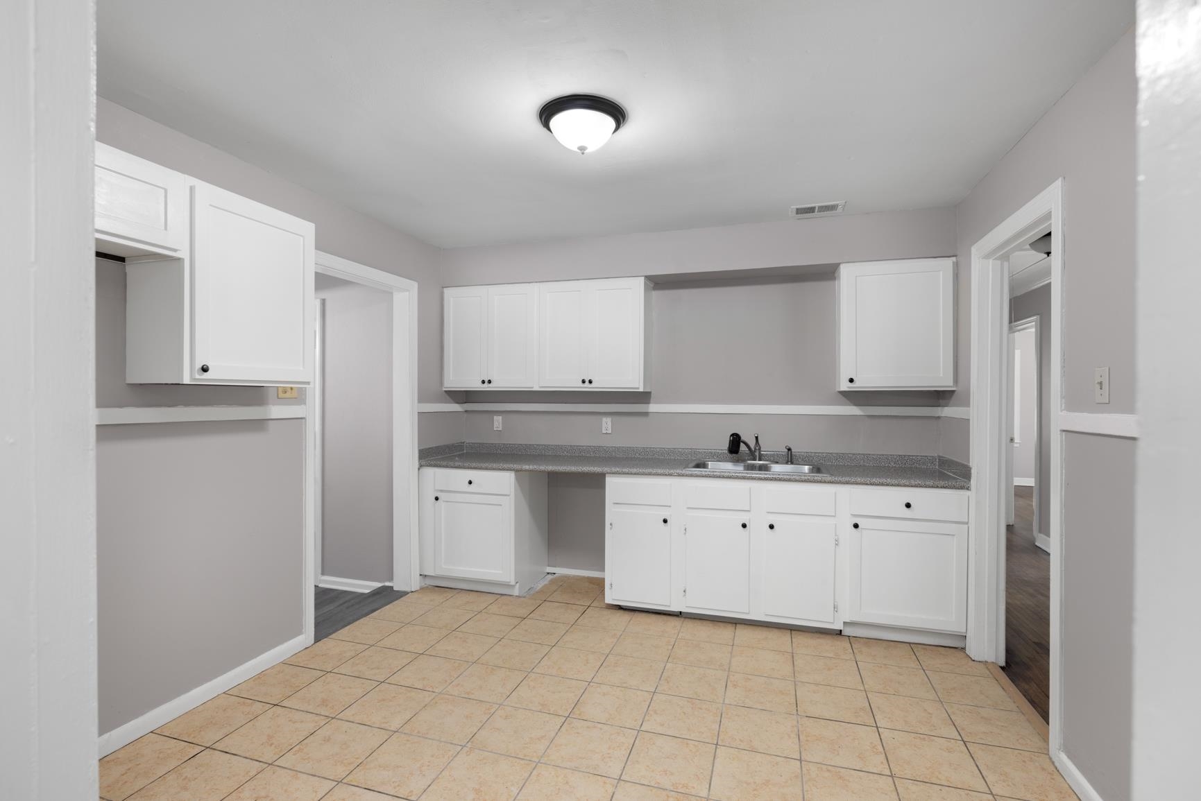 1584 South Perkins Road Memphis, TN 38117 - Photo 11 of 21 Kitchen with light tile patterned floors, baseboards, visible vents, a sink, and white cabinetry