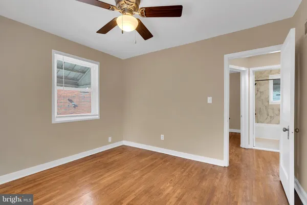 a view of an empty room with wooden floor and a ceiling fan