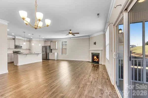 a view of an empty room and kitchen view with wooden floor