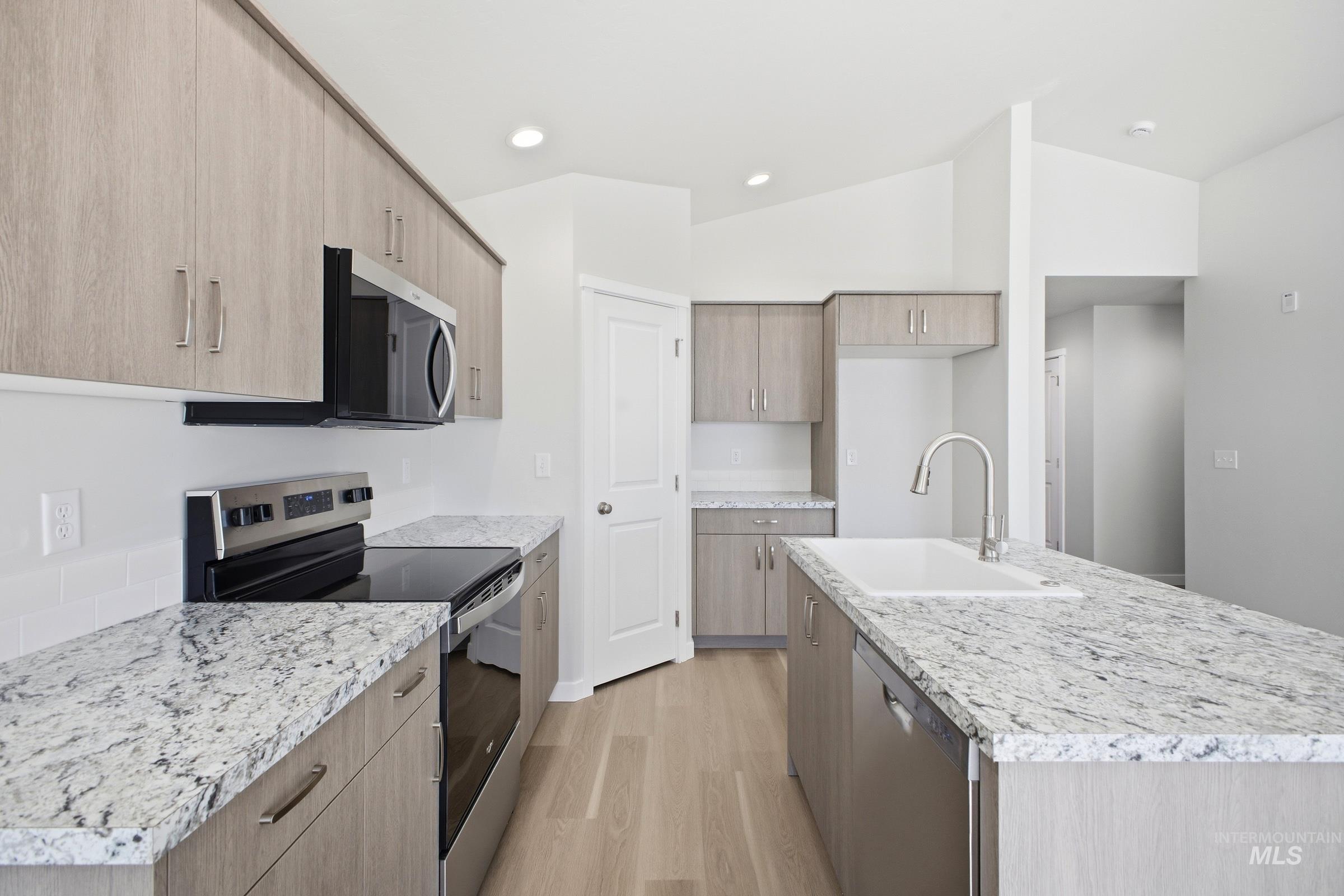 16434 Backfill Avenue Caldwell, ID 83607 - Photo 5 of 19 Kitchen featuring wood-finish cabinetry, granite countertops, stainless steel appliances, a subway tile backsplash, and a large island with an undermount sink