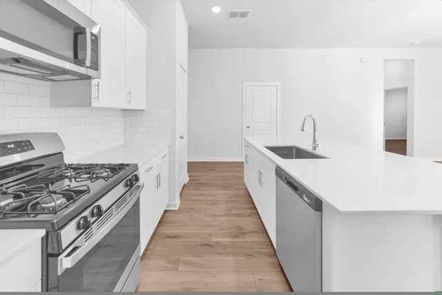 a kitchen with stainless steel appliances a sink a stove a microwave a sink a refrigerator with white cabinets and wooden floor