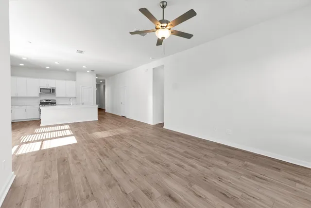 a view of an empty room and window a ceiling fan and wooden floor