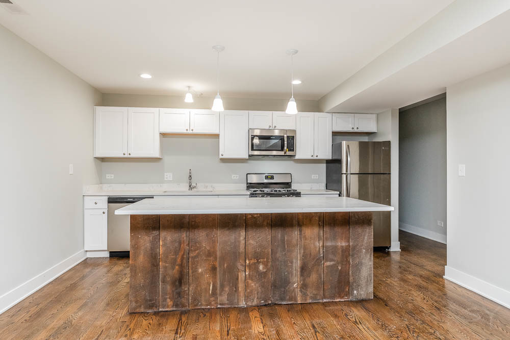 2109 West 18th Place Chicago, IL 60608 - Photo 5 of 63 a large kitchen with kitchen island a sink a stove a refrigerator and white cabinets with wooden floor