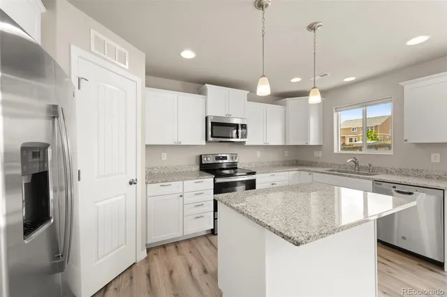 a kitchen with kitchen island granite countertop stainless steel appliances a sink a refrigerator a center island a stove and cabinets