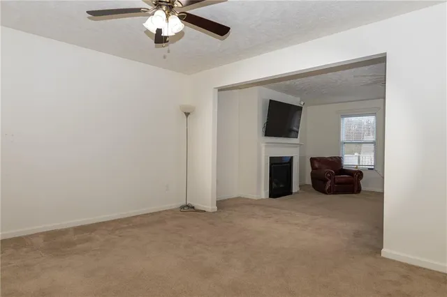 a view of a livingroom with a fireplace a ceiling fan a kitchen and a window
