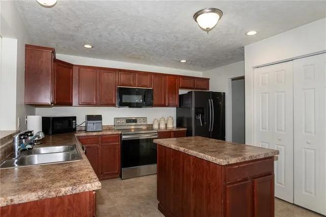 a kitchen with kitchen island granite countertop stainless steel appliances a sink dishwasher a refrigerator a stove top oven and a center island with wooden floor