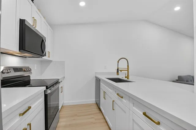 a large kitchen with stainless steel appliances a sink dishwasher and white cabinets with wooden floor